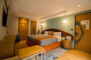 A hotel room with a bed, a desk, a chair, a desk lamp, a bedside table, and a wall-mounted TV. - Hotel Catalina (Mexico City)