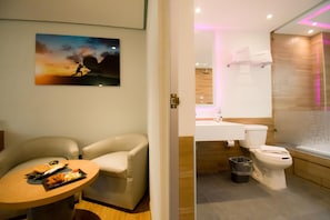 A modern bathroom with a toilet, sink, and shower. There is a painting on the wall and a chair in the room. - Hotel Catalina (Mexico City)