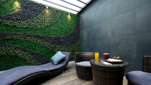 Ein gemütlicher Ruhebereich mit grüner Wand, Korbmöbeln und einem Glastisch mit einem Getränk.