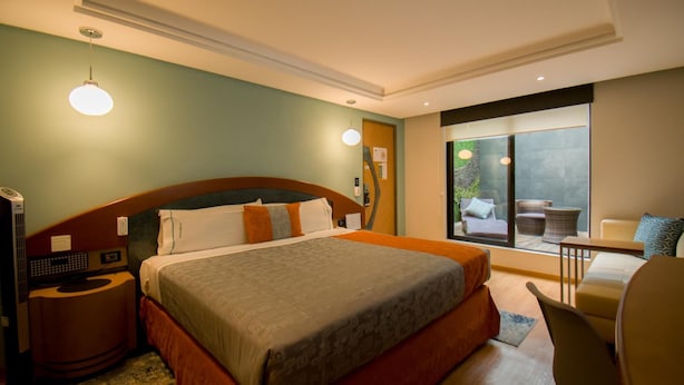 Ein Hotelzimmer mit einem großen Bett, einem Schreibtisch, einem Stuhl und Blick ins Freie.