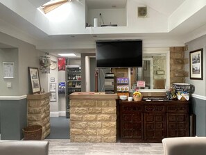 A bar area with a stone counter, a television above, and a refrigerator in the background.