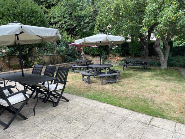 An outdoor patio area with picnic tables and chairs, surrounded by greenery and trees.