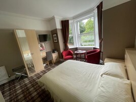 A hotel room with a bed, a desk with a chair, a TV, and a window with curtains.