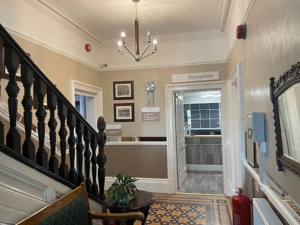 Uma área de recepção de hotel com uma escadaria, um balcão de atendimento e uma placa indicando a recepção.