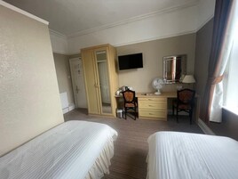 A hotel room with two beds, a desk with a chair, a television, a mirror, and a window with curtains.