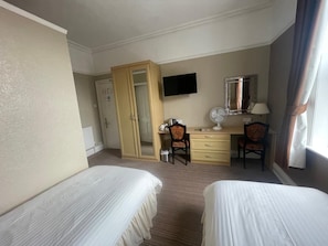 Quarto de hotel com duas camas, uma escrivaninha com cadeira, televisão, espelho e janela com cortinas.