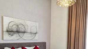 Ein Hotelzimmer mit einem großen Bett, einer modernen Kronleuchter, einem Wandbild und einem fenster mit Vorhängen.