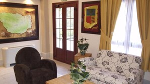 A living room with a sofa, armchair, and a coffee table. There is a map on the wall and a coat rack. - Adeko Hotel (Barakaldo)
