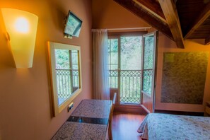 Una habitación con cama, escritorio, silla, televisión y ventana con vista a follaje.