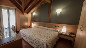 A hotel room with a bed, bedside lamps, a wooden headboard, a desk with a chair, and a window with curtains. - Adeko Hotel (Barakaldo)
