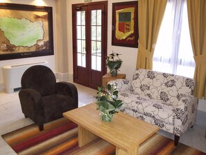 A living room with a sofa, armchair, and a coffee table. There is a map on the wall and a coat rack. - Adeko Hotel (Barakaldo)
