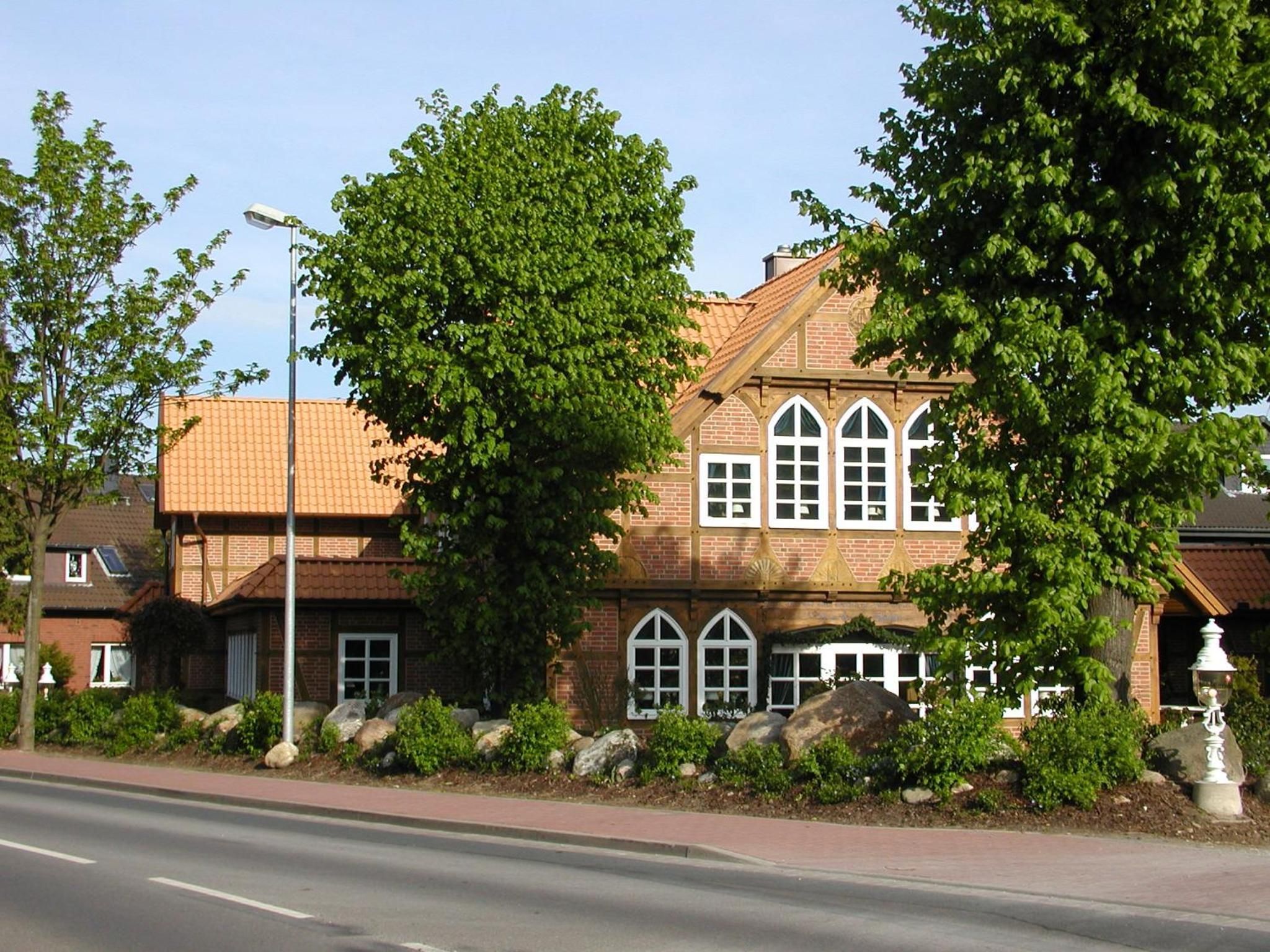Un bâtiment en briques de deux étages, doté d’un toit en tuiles, de grandes fenêtres et d’un jardin bien entretenu agrémenté de rochers et d’arbustes.