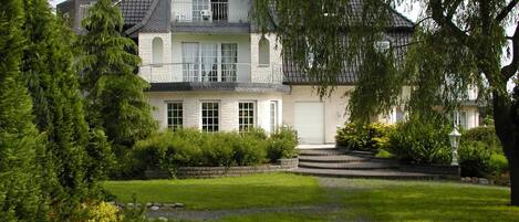 Una casa de dos pisos con un césped cuidado, un camino de entrada de grava y árboles maduros.