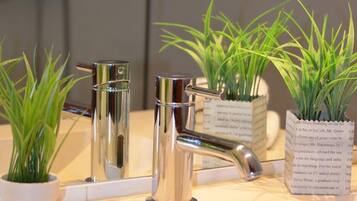 A bathroom with a modern sink, two chrome faucets, and three potted plants.