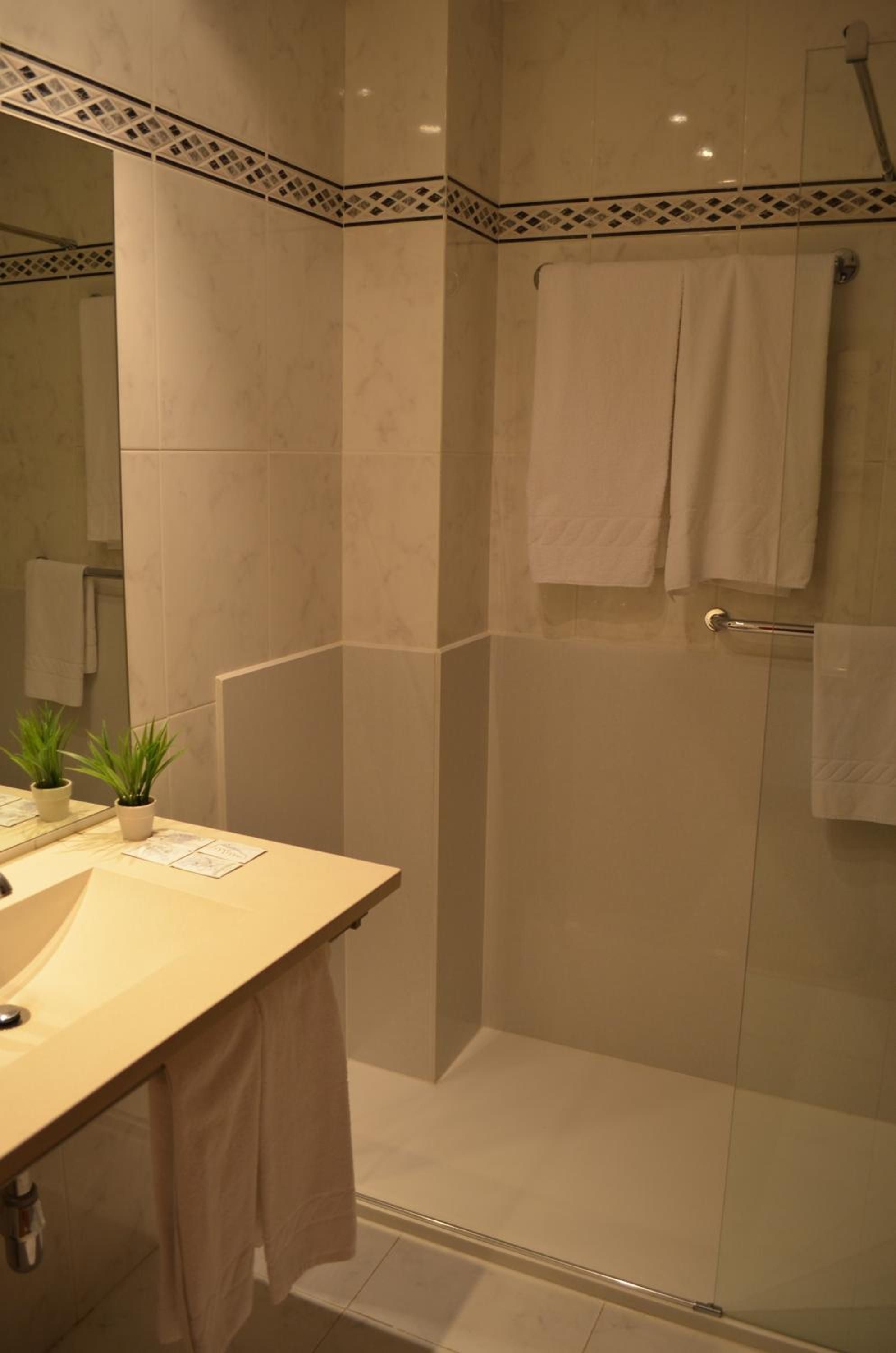Un bany amb dutxa d'estació de vidre, un lavabo amb mirall i un suport per a tovalloles.