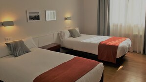 A hotel room with two beds, a nightstand, a wall-mounted lamp, and a window with curtains. - Hotel Elorrio (Elorrio)
