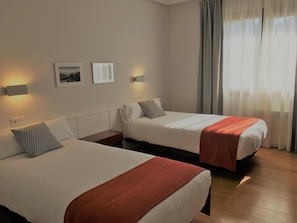 A hotel room with two beds, a nightstand, a wall-mounted lamp, and a window with curtains. - Hotel Elorrio (Elorrio)