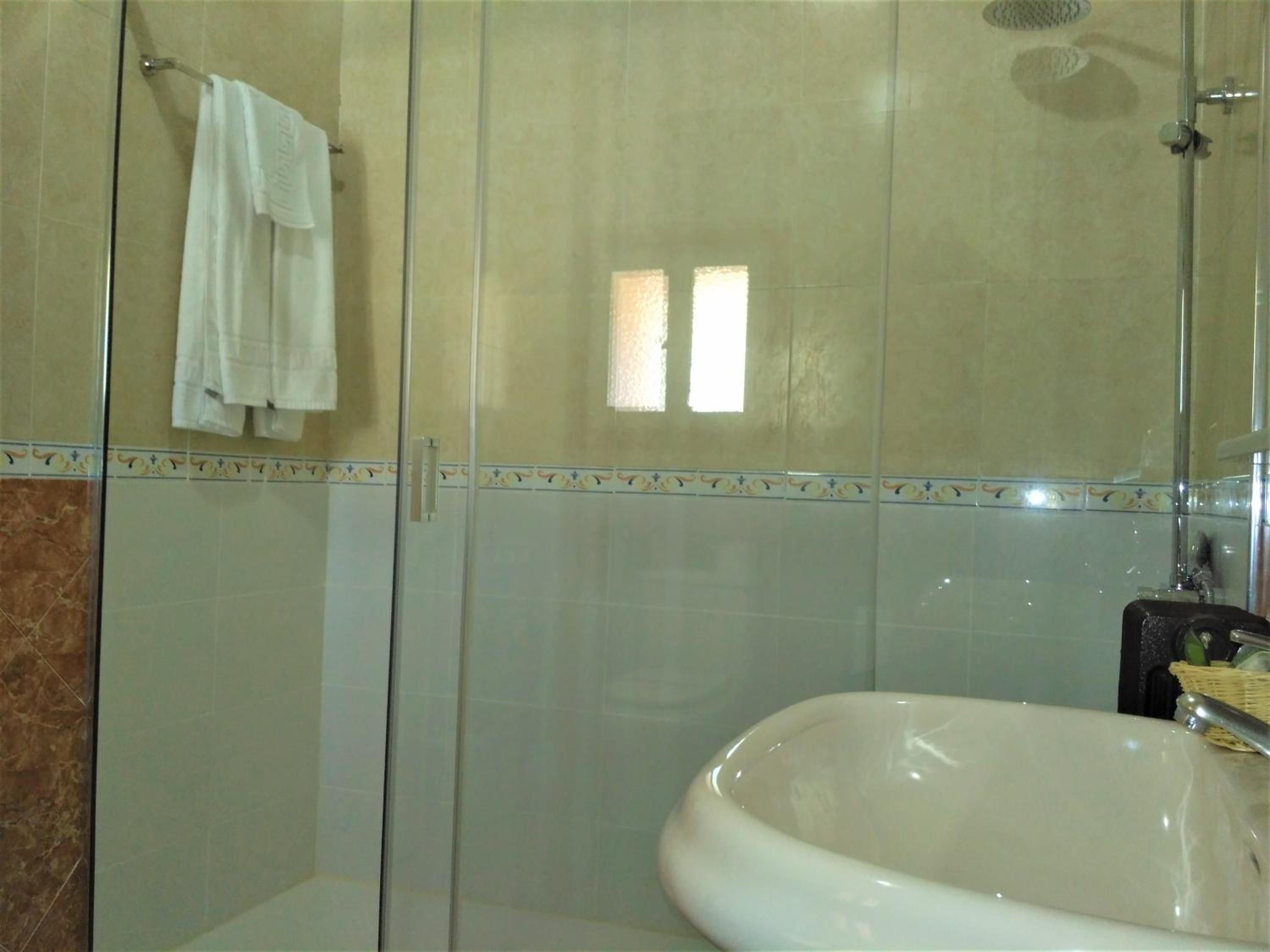 Baño con cabina de ducha de vidrio, lavamanos blanco y pared con un borde decorativo.