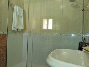Baño con cabina de ducha de vidrio, lavamanos blanco y pared con un borde decorativo.