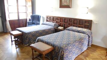 Una habitación de hotel con dos camas, una silla, un banco de madera y un cabecero de madera.