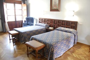 Una habitación de hotel con dos camas, una silla, un banco de madera y un cabecero de madera.