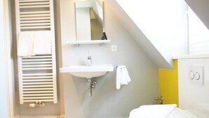Een badkamer met een schuine plafond, een wit wastafelmeubel, een spiegel en een handdoekhouder.