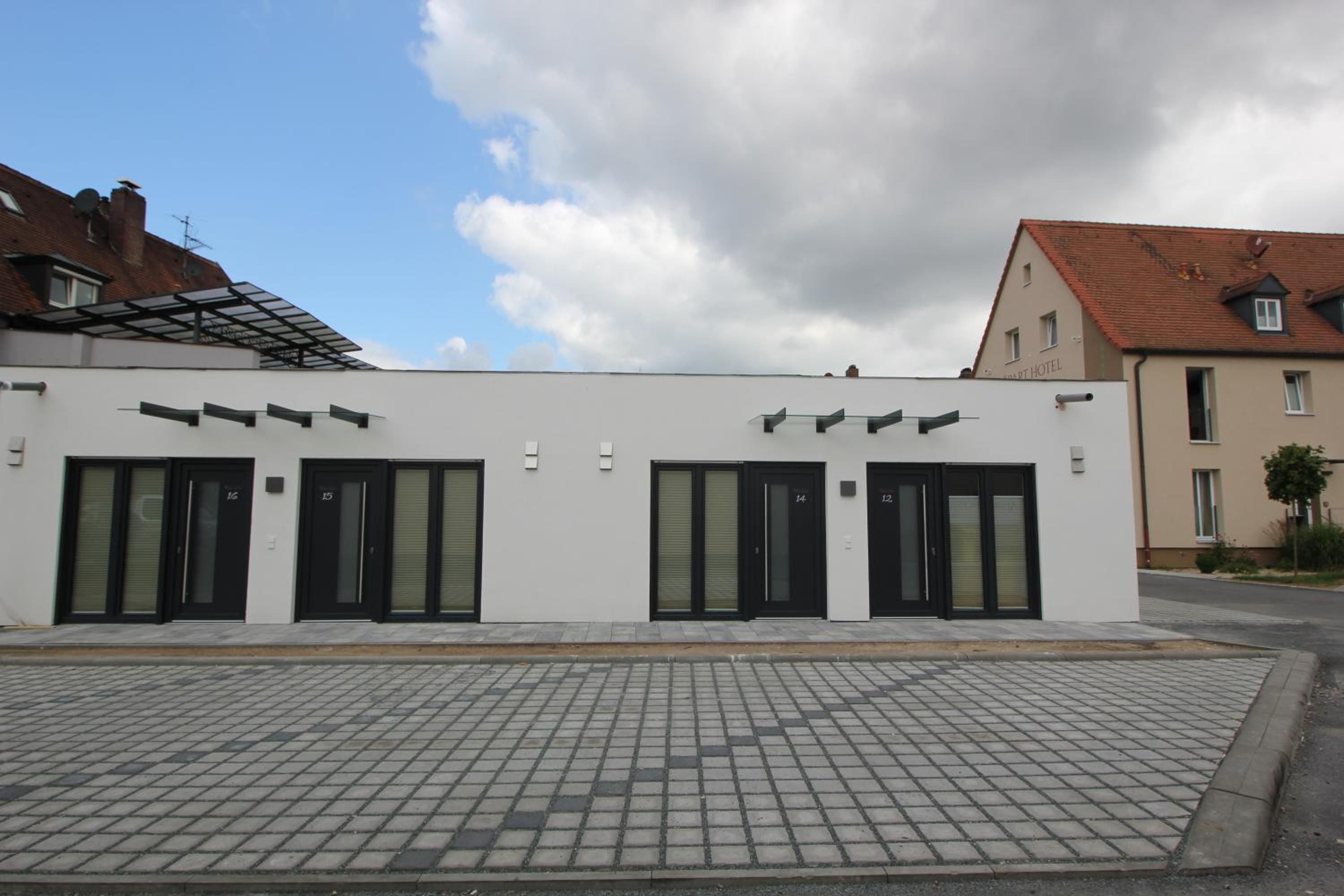 Un edificio moderno con fachada plana, puertas numeradas y un área de entrada pavimentada.