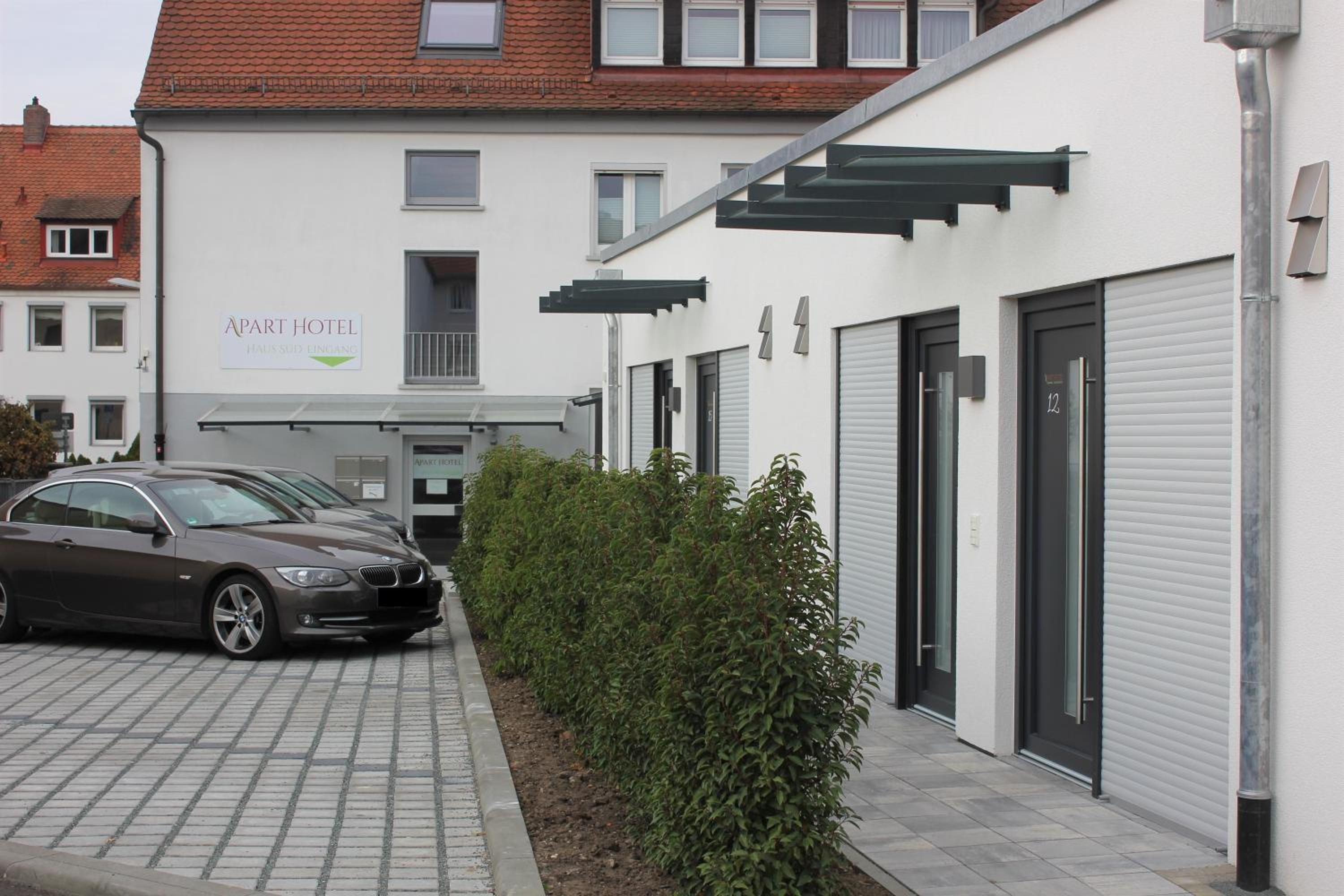 Un bâtiment moderne avec une enseigne indiquant « Appart-hôtel » et une voiture garée.