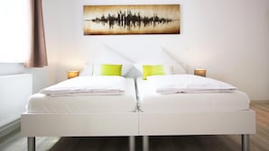 Een tweepersoonsbed met witte beddengoed en twee bedlampjes, een kunstwerk aan de muur en een raam met gordijnen.