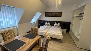 Een kamer met een houten tafel, twee bedden, een stoel en een kledingkast.