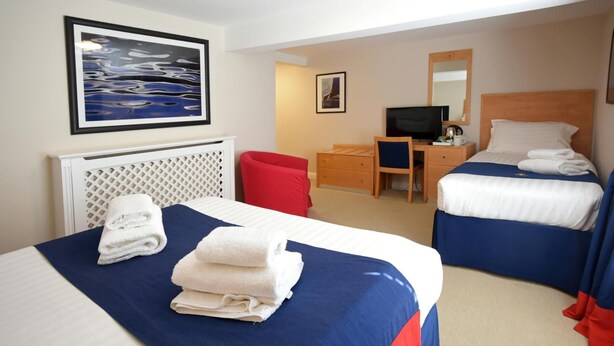 A hotel room with two beds, a desk, a television, and artwork on the walls. - Royal Southern Yacht Club (Southampton)