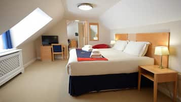 A hotel room with a bed, a desk, a television, and a window.