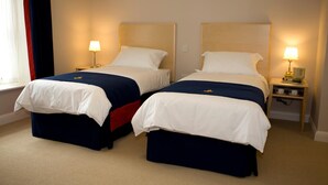 A hotel room with two beds, each with a headboard, bedside tables, and lamps. - Royal Southern Yacht Club (Southampton)