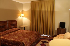 A hotel room with a bed, a television, a lamp, and a window with curtains.