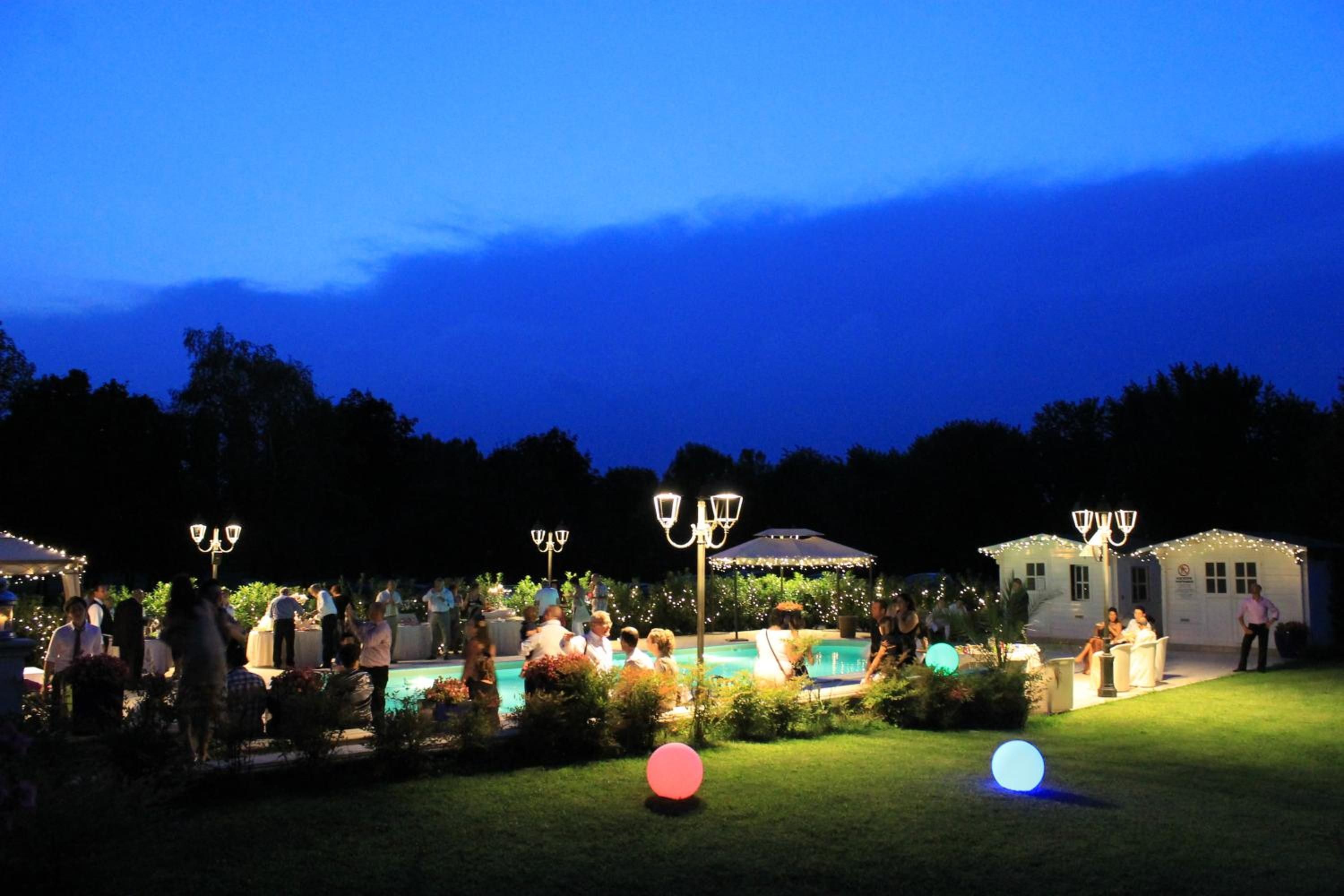 An outdoor gathering with tables and chairs, a pool, and decorative lighting.