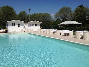 A swimming pool with lounge chairs and umbrellas, surrounded by trees and a building with a sign. - Villa Belvedere 1849 (Misano di Gera d'Adda)