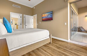 A bedroom with a bed, a painting, and a view of a balcony. - Maui Resort Rentals: Expansive 5BR Ground-Floor Retreat with Three Lawn Areas, Steps from Beach and Pools! (Lahaina)