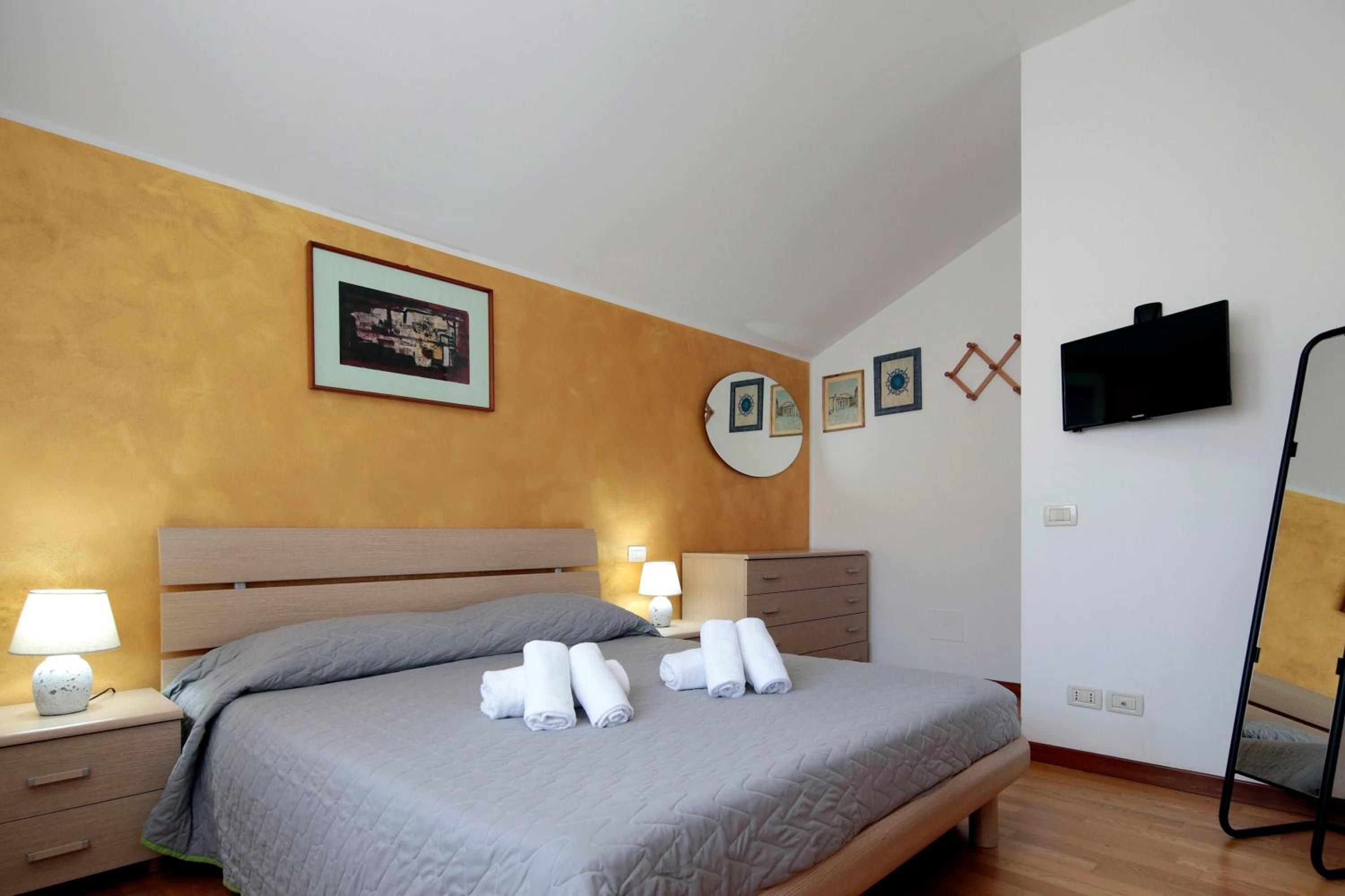 Habitación de hotel con cama, lámparas de noche, televisor de pantalla plana y obras de arte en las paredes.