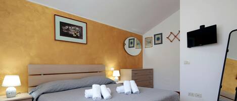 A hotel room with a bed, bedside lamps, a flat-screen TV, and artwork on the walls.