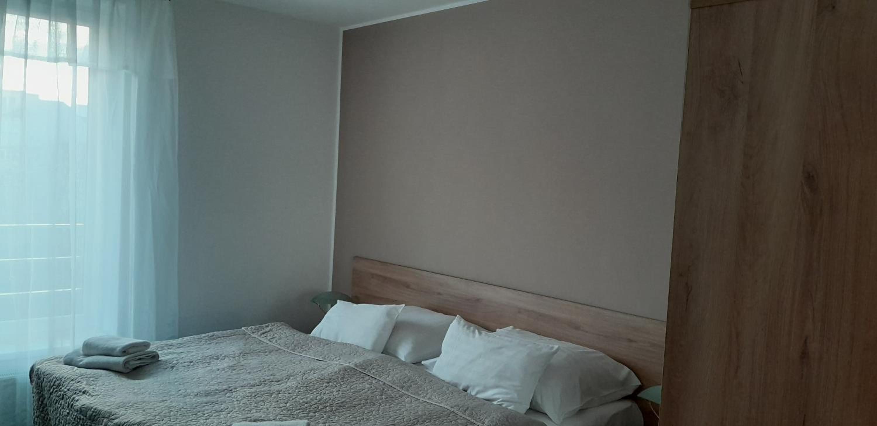 A bedroom with a bed, a wooden headboard, and a window with sheer curtains.