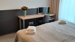 A hotel room with a bed, a desk with a computer, a chair, a vase with flowers, and a window with curtains. - Hotel Aréna (Prague)