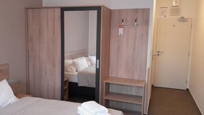A hotel room with a bed, a wardrobe, a shelf unit, and a door. - Hotel Aréna (Prague)