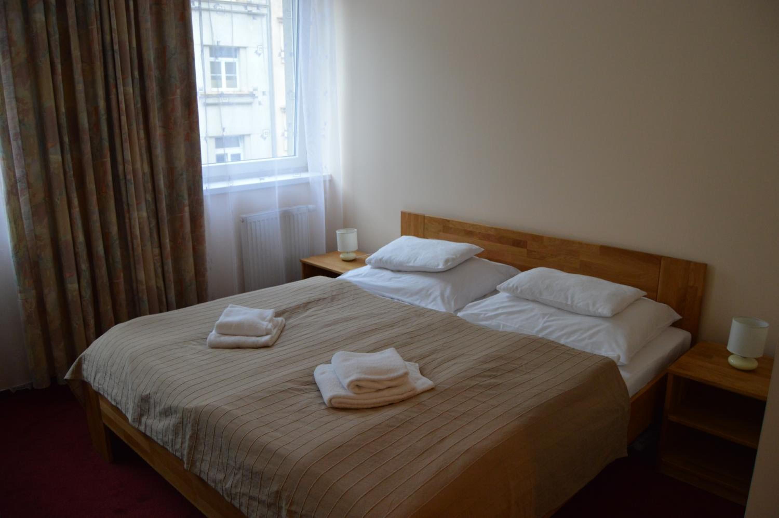 A hotel room with a large bed, two bedside tables, a window with curtains, and a view of buildings outside.