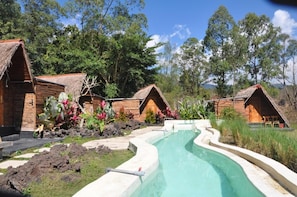 Un área de piscina con cabañas de madera, rodeada de vegetación tropical.