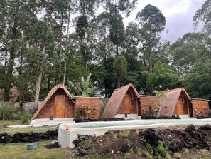 A row of wooden cabins with pitched roofs, surrounded by a pool and lush greenery.