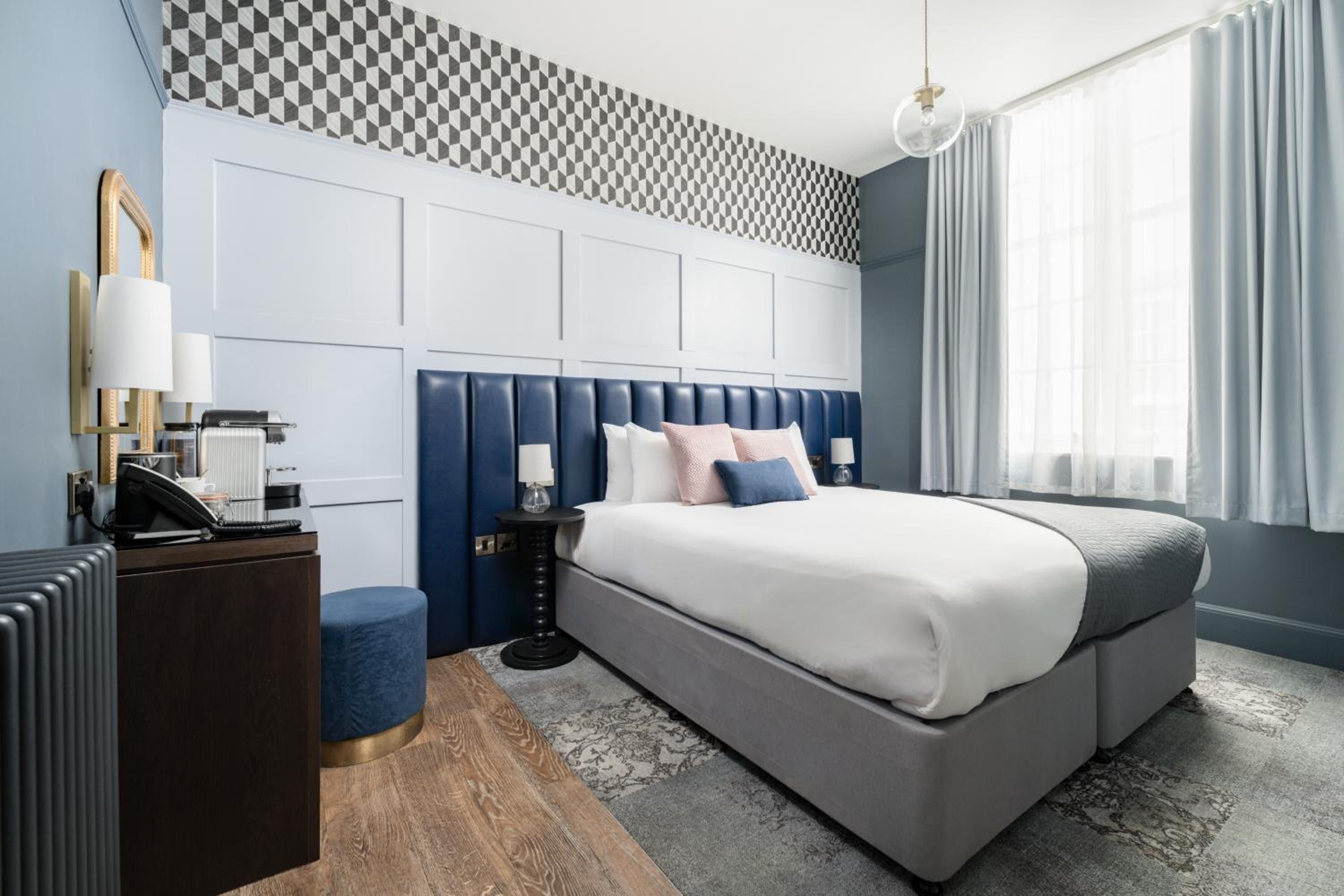 A modern hotel room with a large bed, a desk, and a patterned wall.