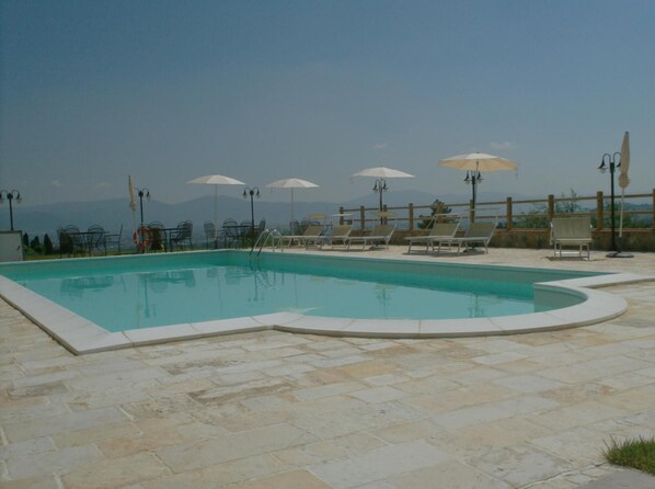 A swimming pool with lounge chairs and umbrellas, surrounded by stone tiles. - Poggio Desto Bed & Breakfast (Quarrata)