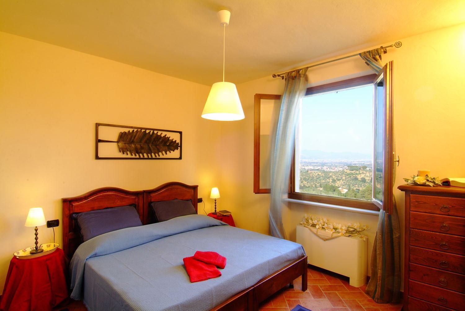Un dormitorio con una cama, lámparas de noche, una ventana con vistas y un aparador de madera.