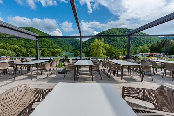 An outdoor dining area with tables and chairs, overlooking a lake and mountains.