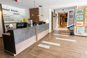 Zona de recepción de hotel con un diseño moderno, que incluye un mostrador de recepción, un bar de café y un cartel para una sala de conferencias.